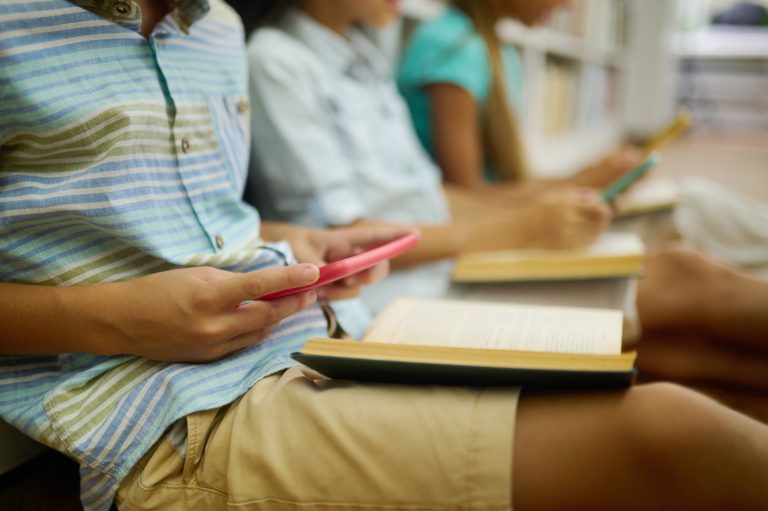 Boy sitting with book enthusiastically engaged in smartphone